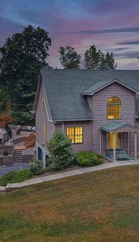 Aerial dusk view of cabin with pool, hot tub, and sports court surrounded by trees