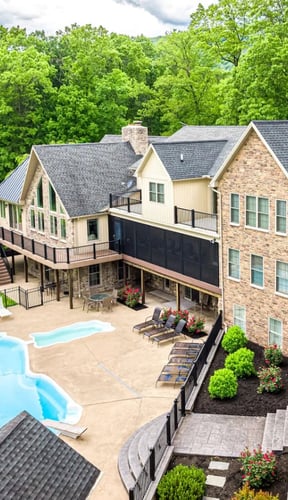 Aerial view of large stone and siding lodge with freeform pool and manicured grounds