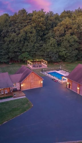 Aerial dusk view of large cabin compound with pool, sports court, and string lights