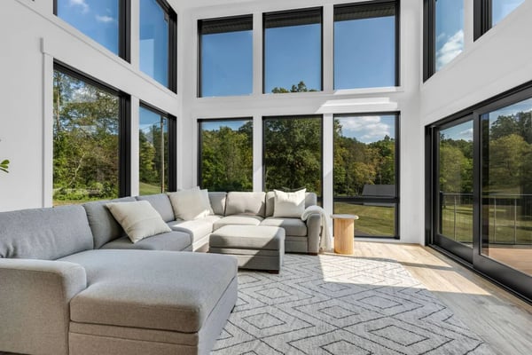 Modern farmhouse with stone foundation, two-story deck, turquoise Adirondack chairs, and manicured lawn at sunset