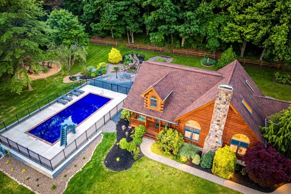 Aerial view of log cabin with pool, hot tub, and manicured grounds surrounded by trees